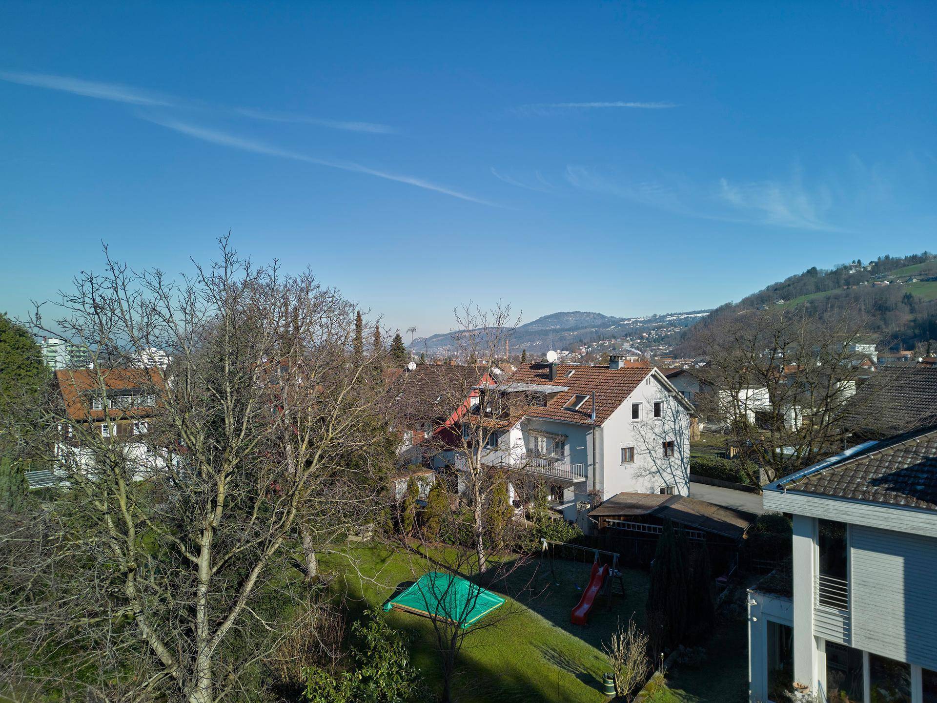 Panoramablick über eine Wohnsiedlung mit Häusern, Bäumen und einem kleinen Spielbereich im Grünen.