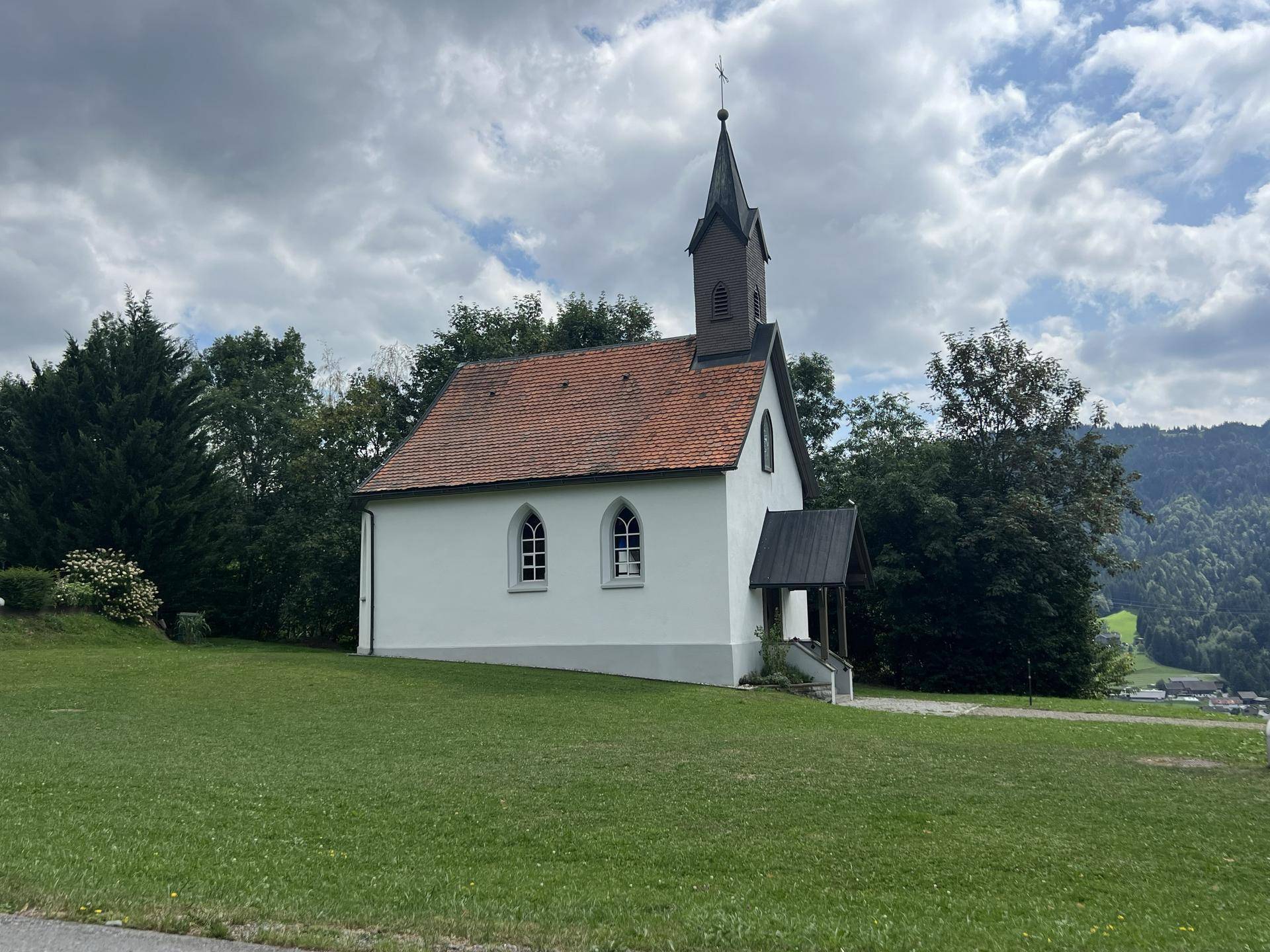 Malerische kleine Kapelle mit rotem Dach und Glockenturm, umgeben von grünen Wiesen.