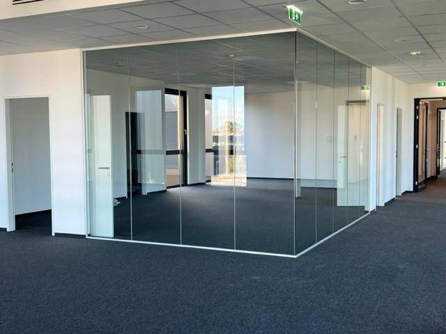 Moderner Bürobereich mit raumhohen Glaswänden, die separate Arbeitsbereiche im Großraumbüro schaffen.