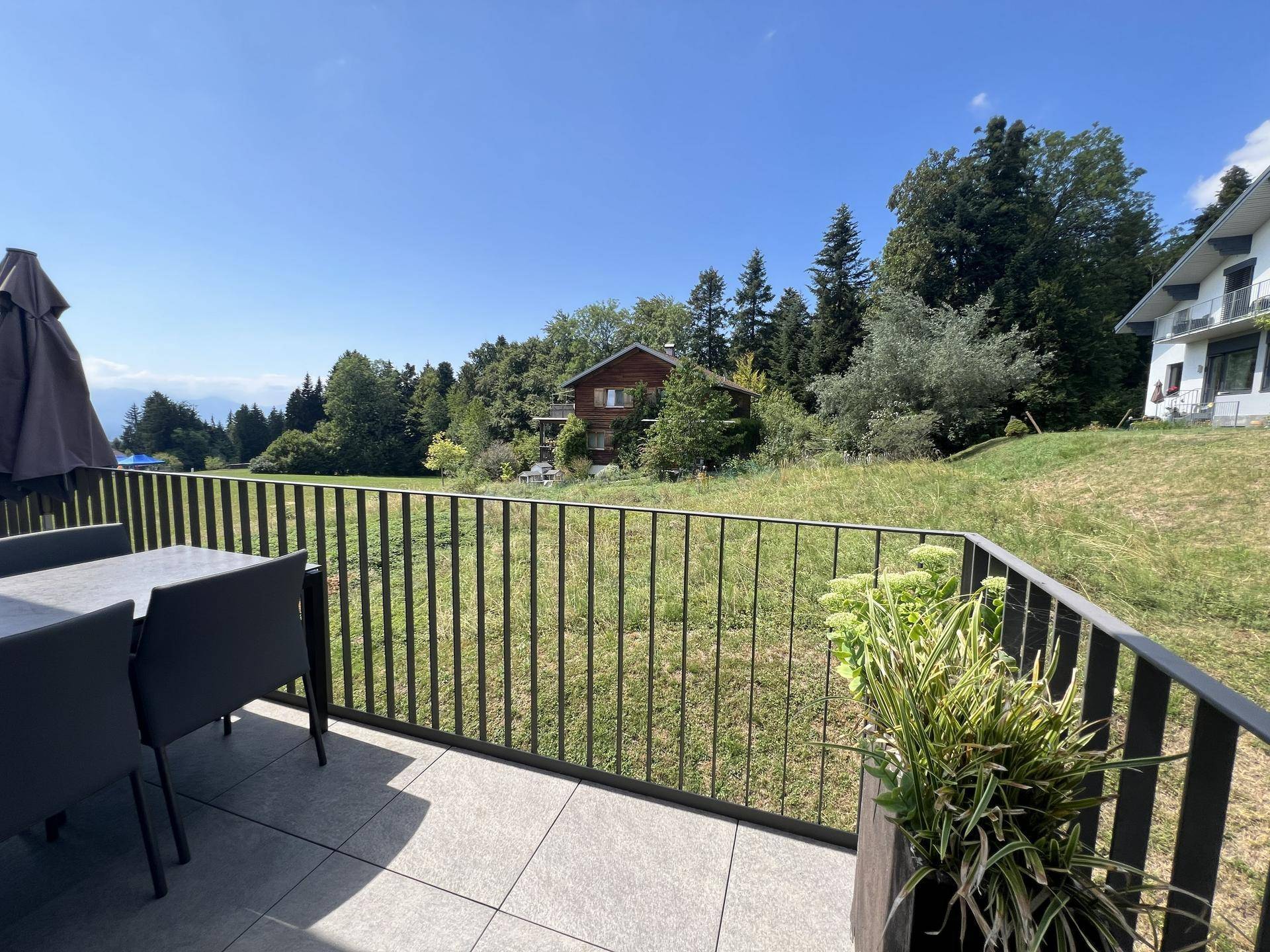 Großer Balkon mit Esstisch und Stühlen, bietet einen weiten Blick über grüne Felder.