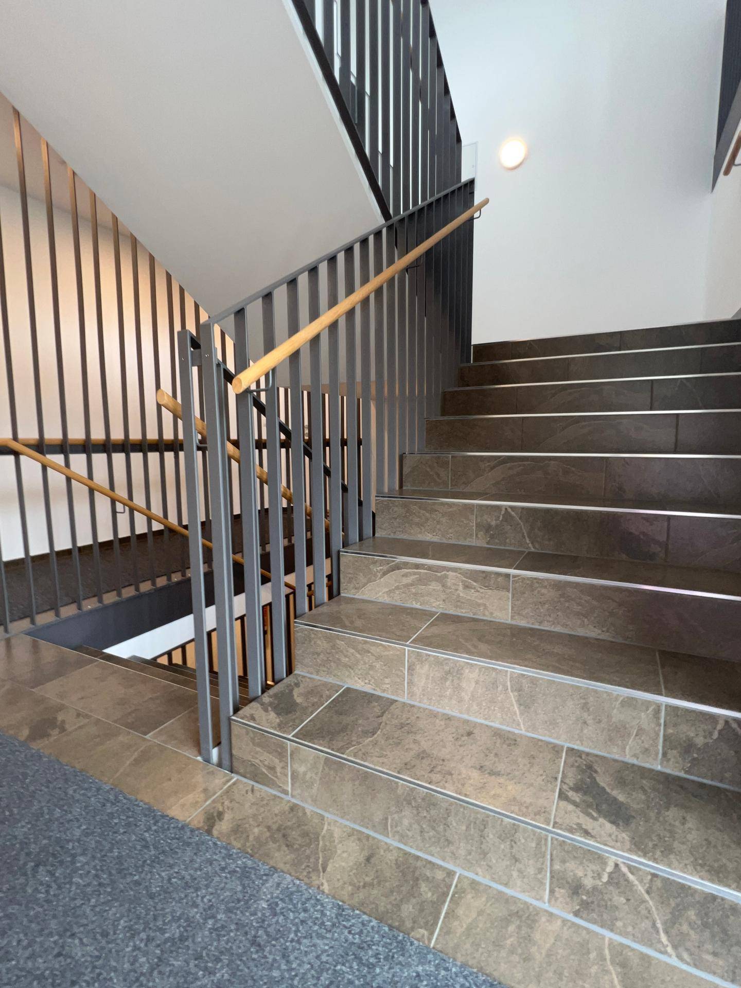 Detailansicht des modernen Treppenhauses mit grauen Fliesenstufen und elegantem Metallgeländer.
