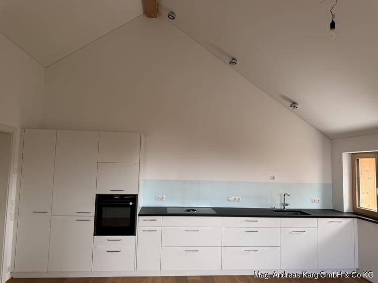 Helle, moderne Einbauküche mit weißen Fronten, dunkler Arbeitsplatte und Dachschräge in einem Neubau.