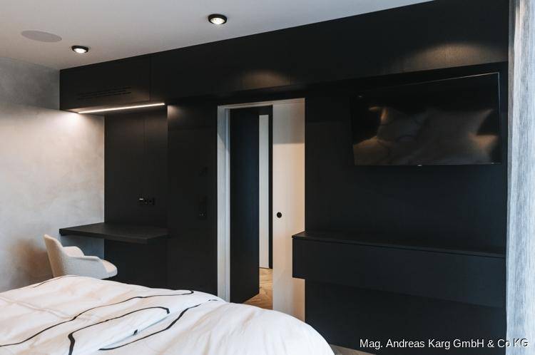 Modernes Schlafzimmer mit großem Bett, integrierten schwarzen Möbeln und Wandfernseher.