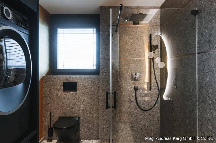Modernes Badezimmer mit begehbarer Dusche, schwarzer Toilette und integrierter Waschmaschine.
