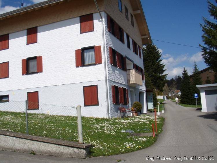 Gepflegtes Wohnhaus mit weißer Fassade, roten Fensterläden und kleinem Balkon.