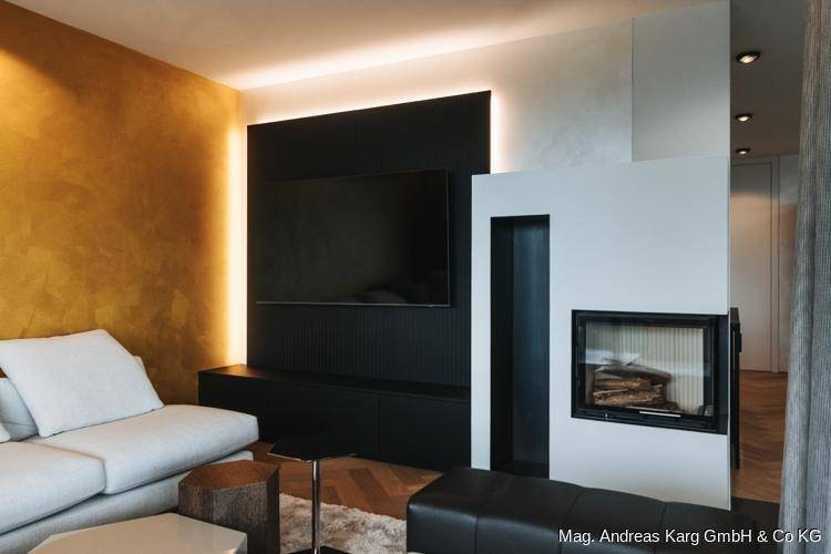 Modernes Wohnzimmer mit Kamin, großem Fernseher und einer auffälligen goldenen Akzentwand.