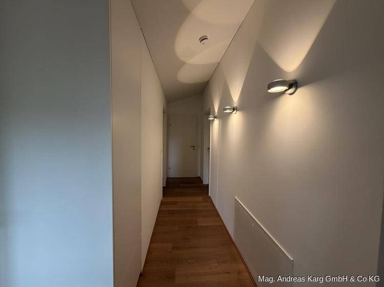 Schmaler, heller Flur mit Holzboden und modernen Wandleuchten, der zu den Wohnbereichen führt.