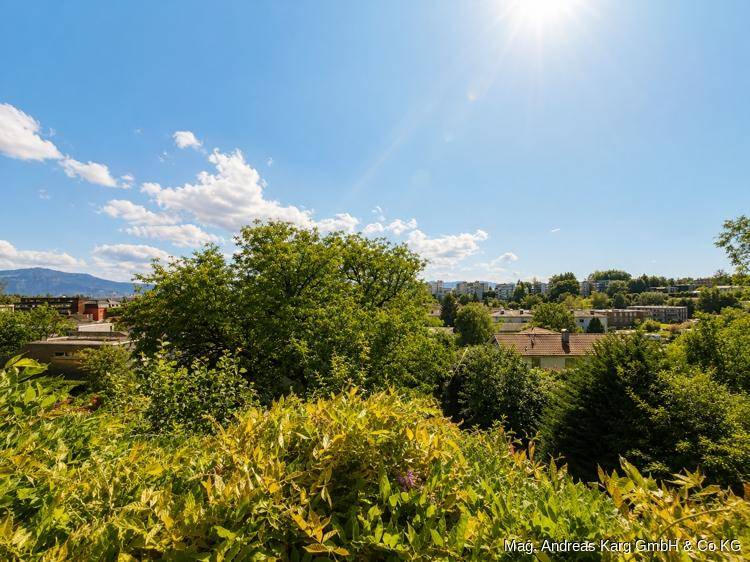 Weitläufiger Ausblick über die Stadt und die umliegende grüne Landschaft an einem sonnigen Tag.