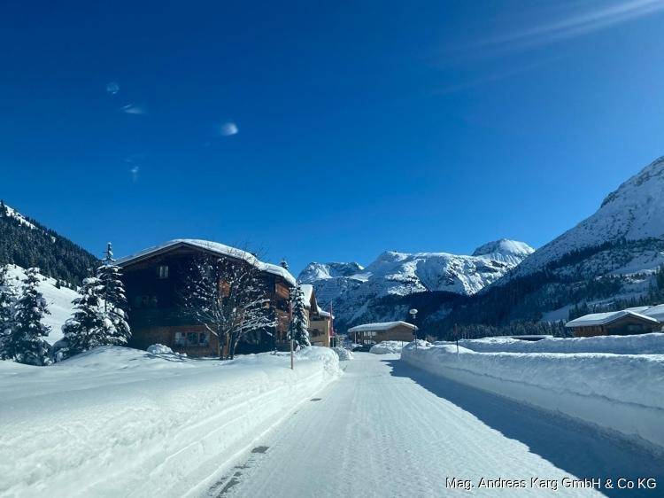 Weite Winterlandschaft mit schneebedeckten Bergen, traditionellen Häusern und einer verschneiten Straße.