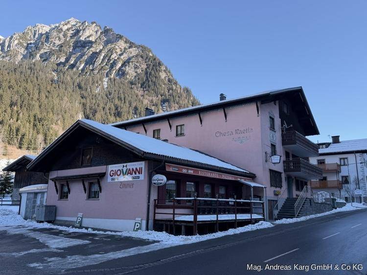 Gebäude mit rosa Fassade, Holzelementen und einem Restaurantbereich, umgeben von Bergen und Schnee.