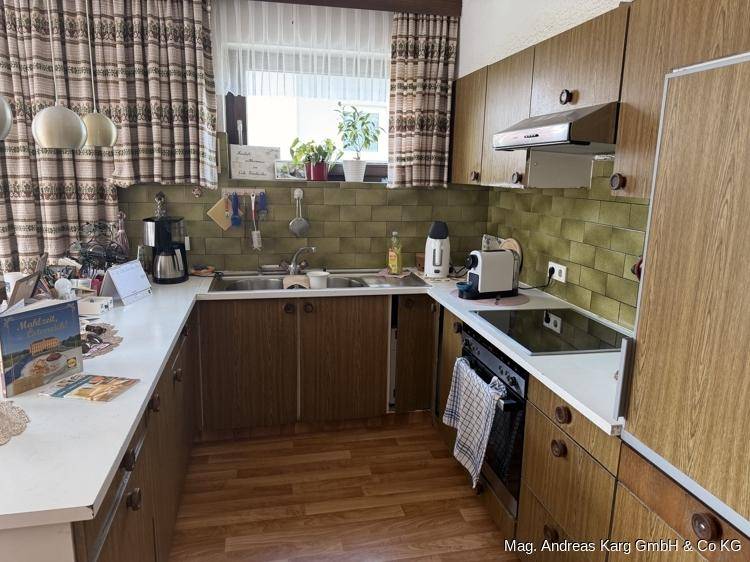 Traditionelle Küche mit Holzschränken, grünen Fliesen und einem Fenster mit Vorhängen.