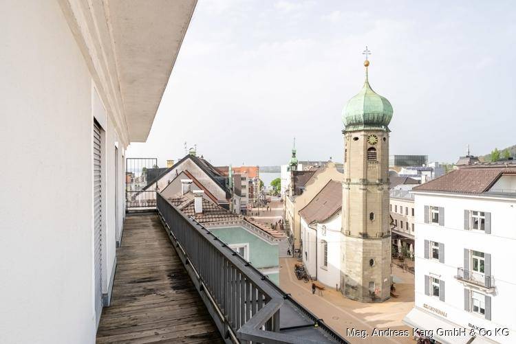 Schmaler Balkon mit Holzboden und Geländer, bietet einen Blick auf den Kirchturm und die Stadt.
