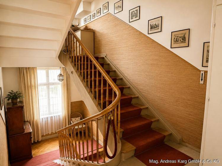 Elegantes Treppenhaus mit Holzgeländer, rotem Teppich und gerahmten Bildern an der Wand.