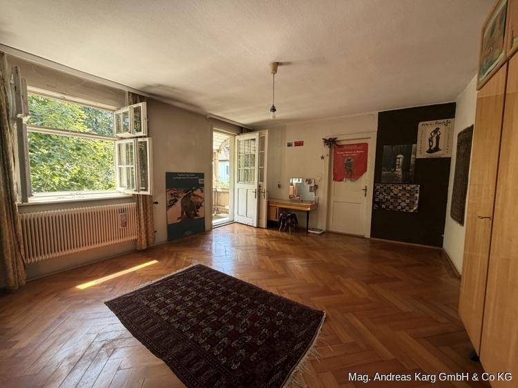 Geräumiges Zimmer mit Fischgrätparkett, Balkonzugang und Blick ins Grüne.