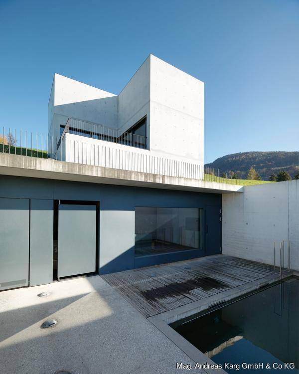 Außenbereich mit Holzdeck, kleinem Wasserbecken und moderner Betonarchitektur im Hintergrund.