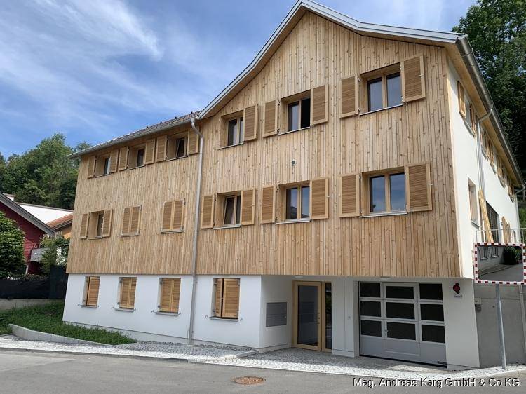 Attraktives Holzhaus mit weißem Sockelgeschoss und integrierter Garage, präsentiert sich in neuwertigem Zustand.