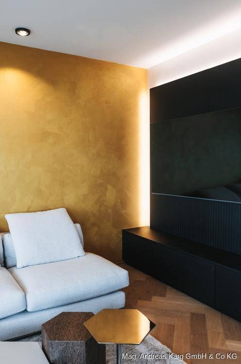 Detailansicht des Wohnzimmers mit goldener Akzentwand, bequemer Couch und indirekter Beleuchtung.