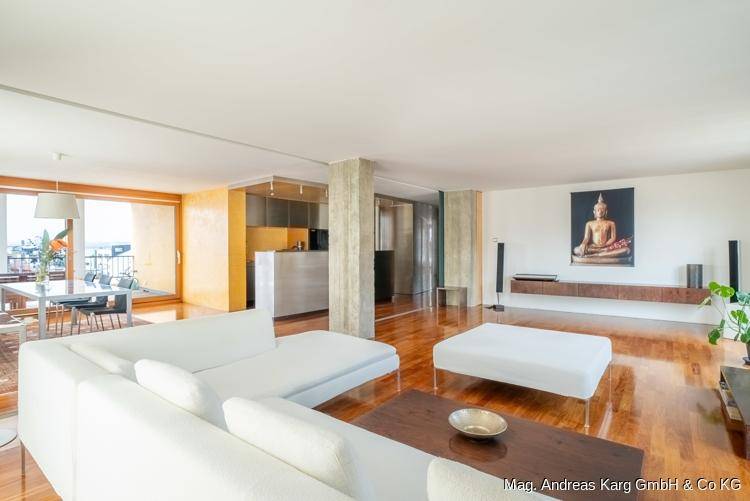 Offener Wohnbereich mit Holzboden, weißem Sofa und Blick auf die moderne Küche.