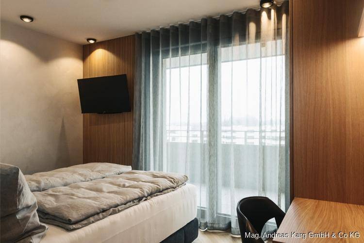 Helles Schlafzimmer mit zwei Betten, Holzwandverkleidung und Zugang zu einem Balkon.