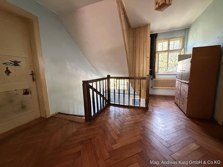 Dachgeschosszimmer mit Fischgrätparkett, Dachschräge und Blick ins Grüne.