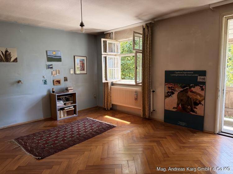 Freundliches Zimmer mit Fischgrätparkett, blauer Wand und Blick ins Grüne.
