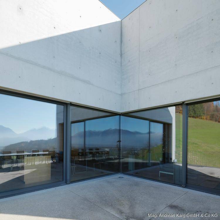 Moderne Glasfassade mit großen Fenstern, die die umliegende Landschaft widerspiegeln.