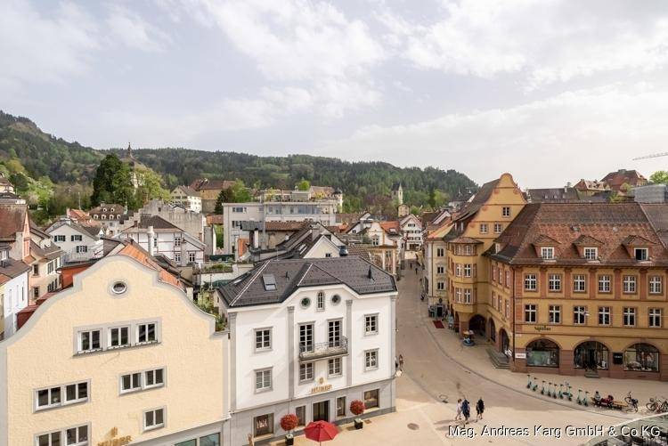 Blick auf eine charmante Stadtstraße mit historischen und modernen Gebäuden vor grünen Hügeln.