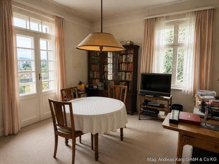 Gemütlicher Wohnraum mit Bücherregal, Esstisch und Zugang zu einem französischen Balkon.