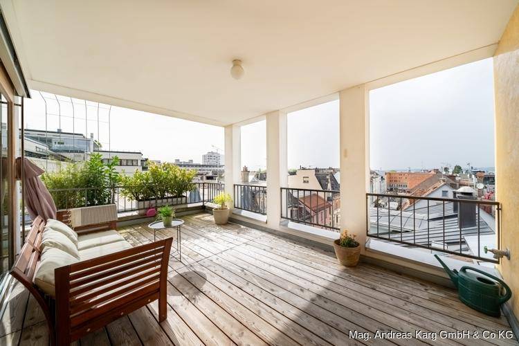 Geräumiger Balkon mit Holzdeck, Sitzgelegenheiten und Blick über die Stadt.