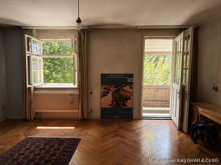 Helles Zimmer mit Fischgrätparkett, Fenster und Balkonzugang, umgeben von Grün.