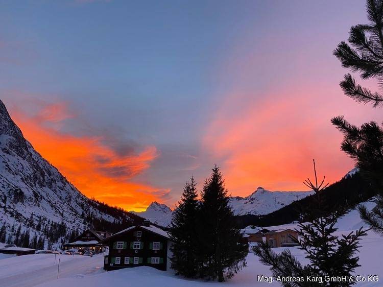 Spektakulärer Sonnenuntergang über einer verschneiten Berglandschaft mit leuchtendem Himmel und Chalets.