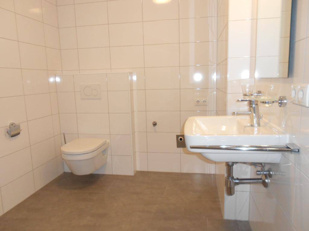 Modernes Badezimmer mit weißen Wandfliesen, grauem Boden, wandhängendem WC und Einzelwaschbecken.