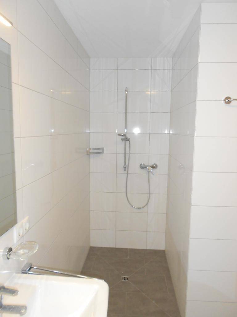Modernes Badezimmer mit weißen Fliesen, grauem Boden und einer begehbaren Dusche.