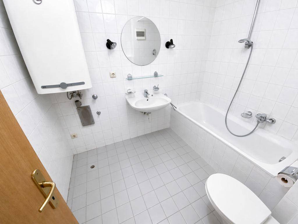 Helles Badezimmer mit Badewanne, integrierter Dusche und weißen Wand- und Bodenfliesen.