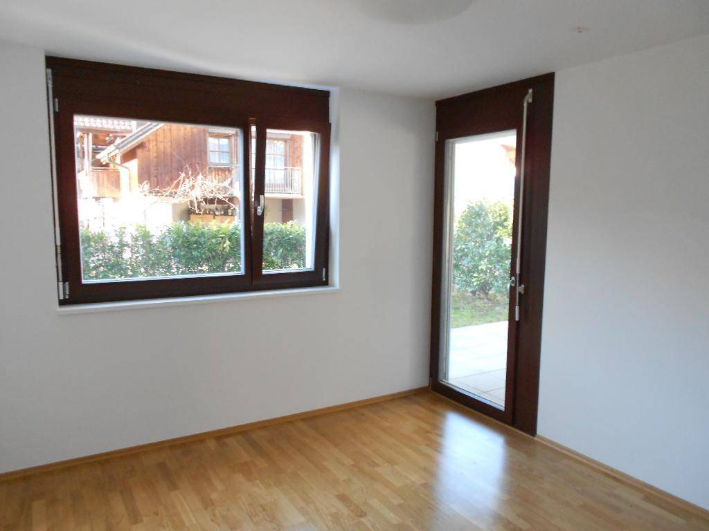 Helles Zimmer mit Parkettboden, Fenster und Zugang zu einem Außenbereich.