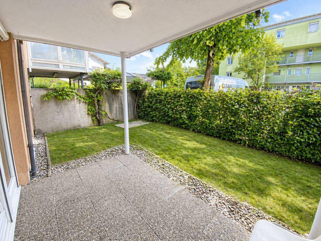 Überdachte Terrasse mit angrenzendem Rasen und einer hohen Hecke als Sichtschutz.