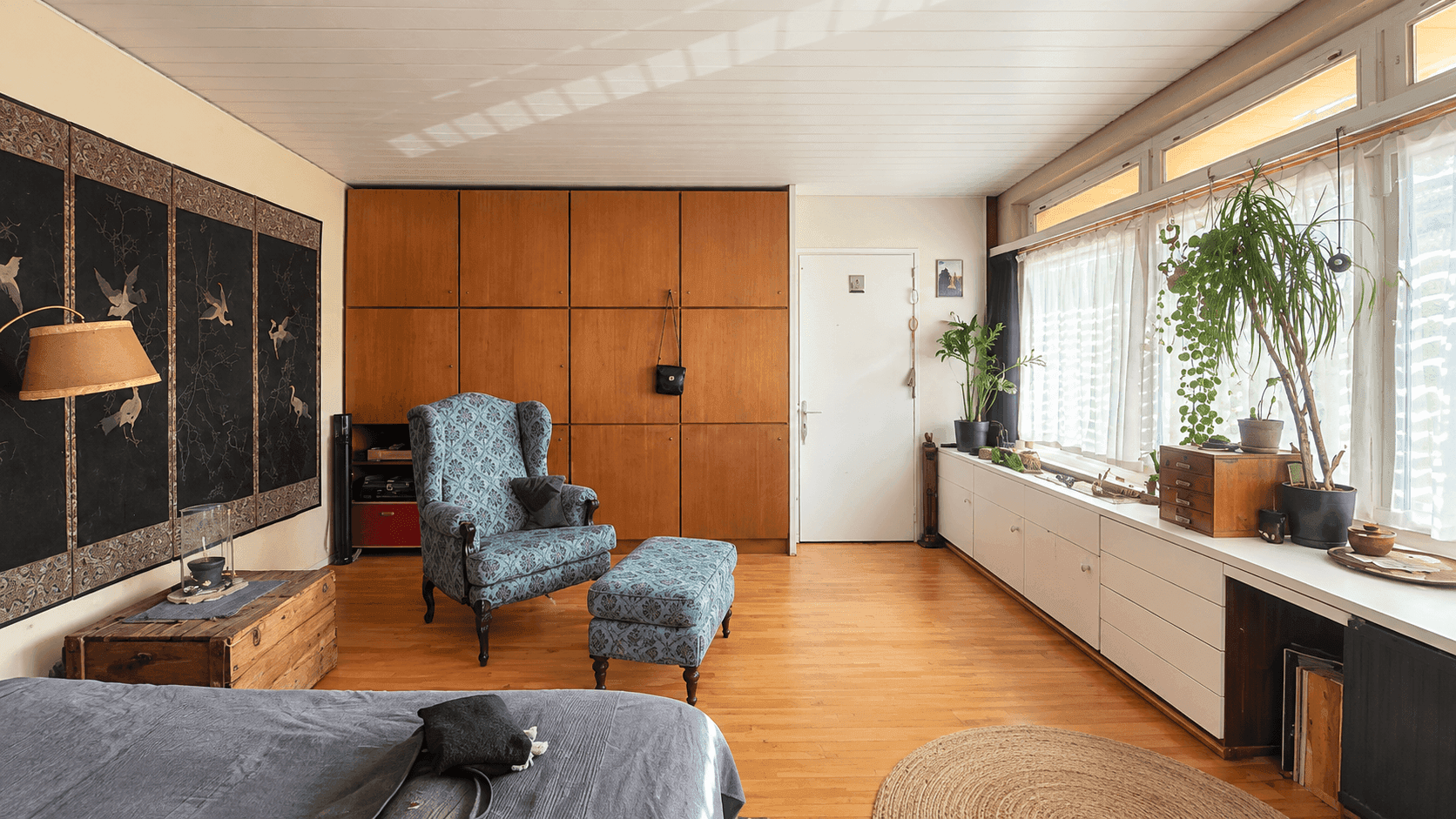 Gemütliches Schlafzimmer mit Holzwänden, einem Bett und einer langen Fensterbank mit Stauraum.