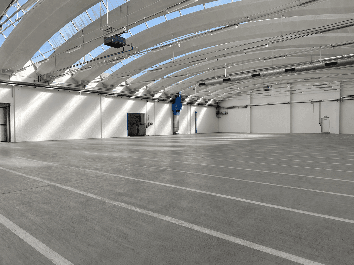 Helle und weitläufige Lagerhalle mit Betonboden, hohen Decken und Oberlichtern für optimale Beleuchtung.