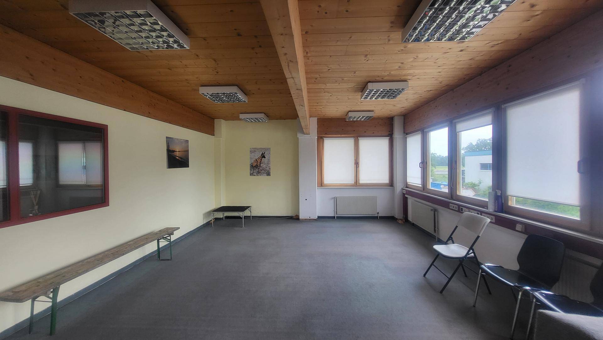 Heller Büroraum mit Holzbalkendecke, großen Fenstern und Blick ins Grüne, ausgestattet mit Sitzgelegenheiten.