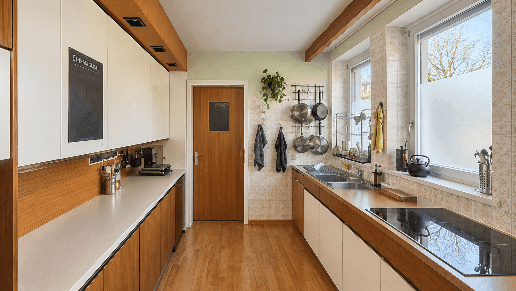 Funktionale Küche mit weißen und holzfarbenen Schränken, Parkettboden und zwei Fenstern.