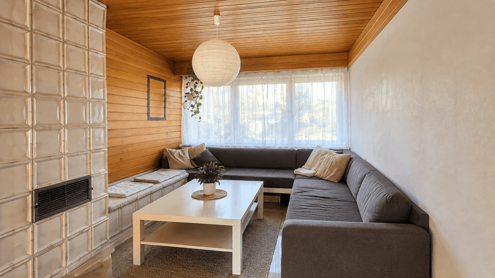 Wohnzimmer mit großem Ecksofa, Kachelofen, Holzvertäfelung und viel natürlichem Licht.