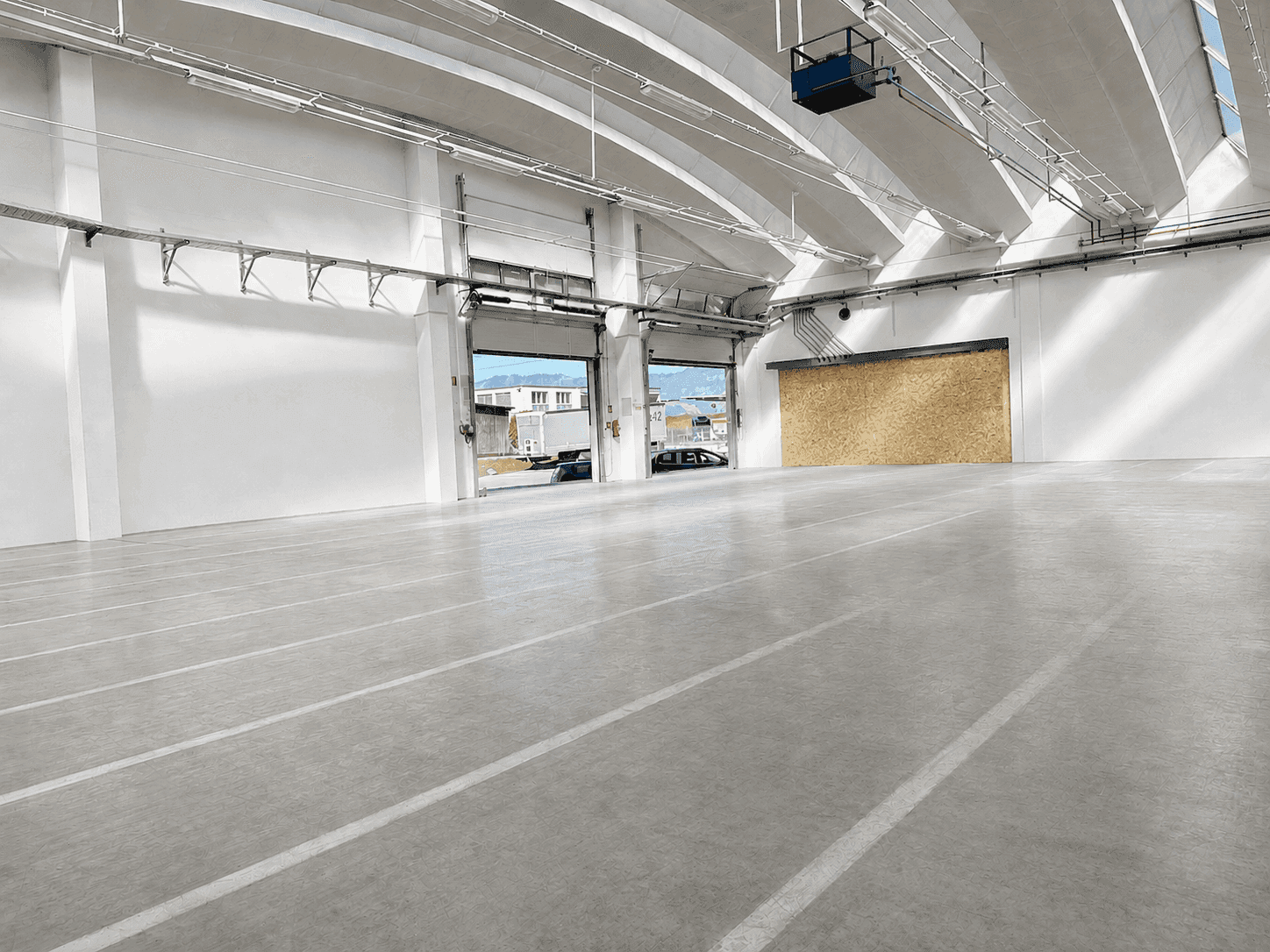 Geräumige Lagerhalle mit Betonboden, hohen Decken und zwei großen Rolltoren, eines davon verkleidet.