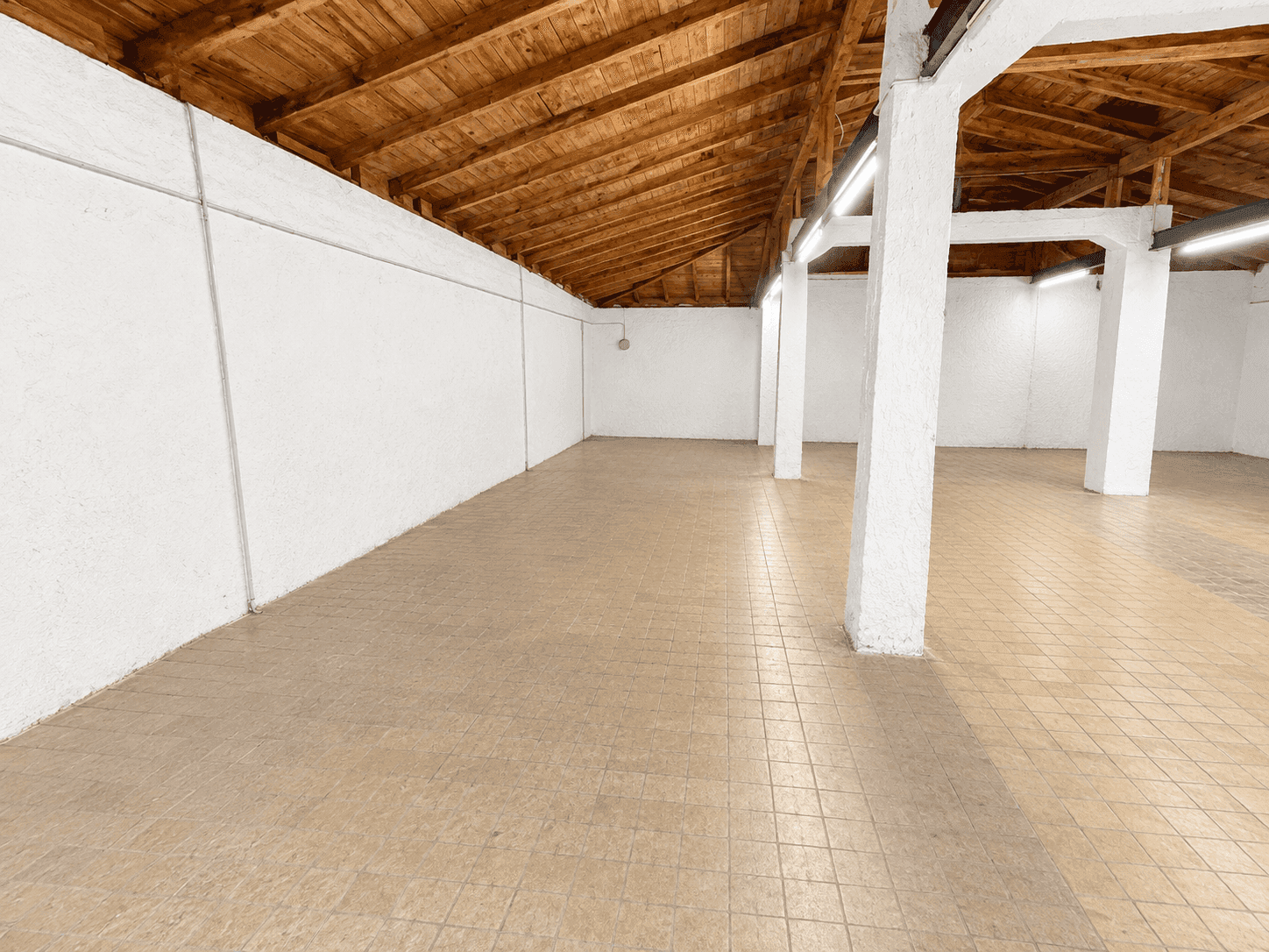 Heller Gewerberaum mit weiß gestrichenen Wänden, Säulen und einer Holzsparrenkonstruktion an der Decke.