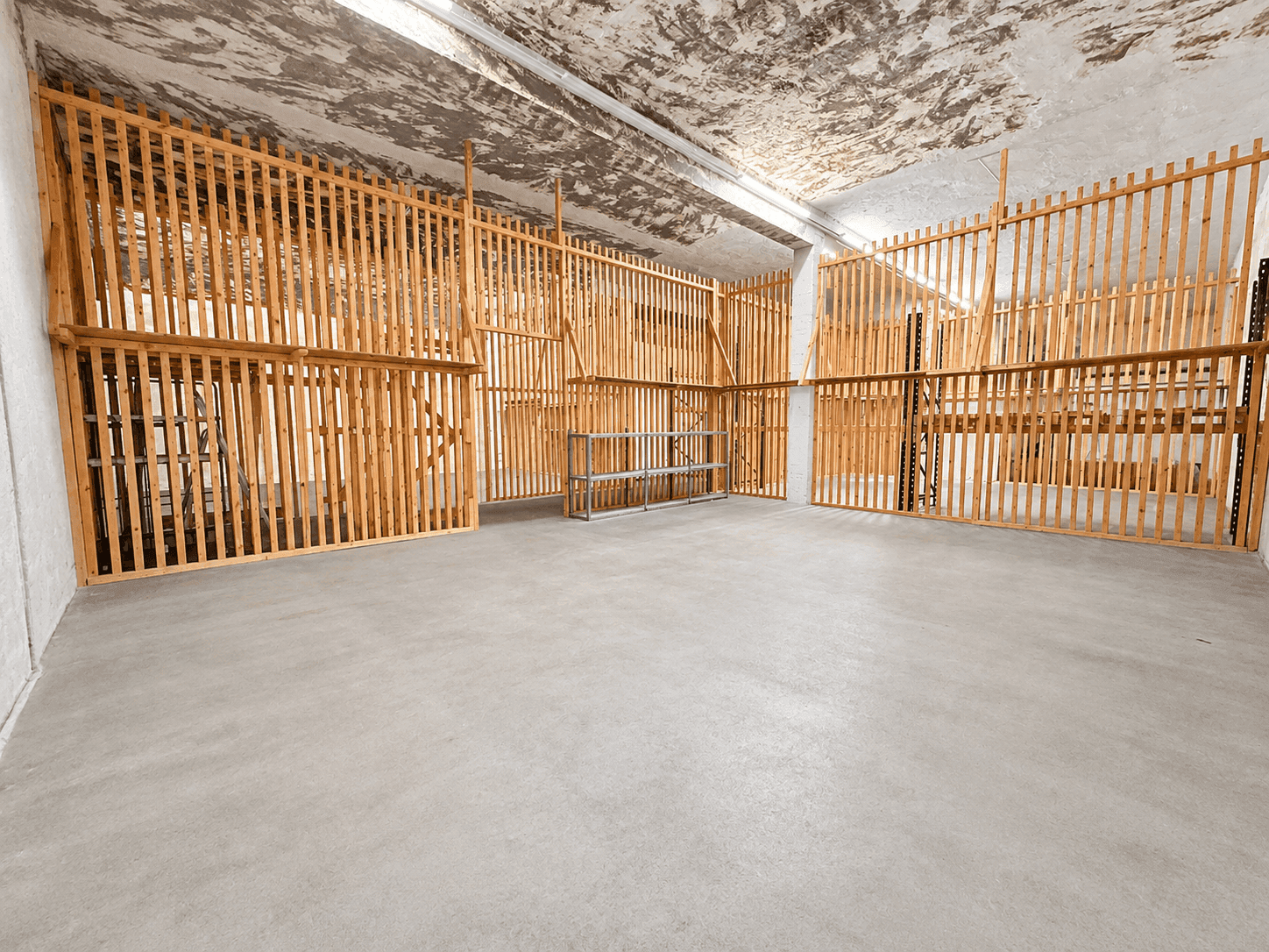 Großer Lagerraum mit Betonboden und vielen Holzabtrennungen, die separate Lagereinheiten bilden.