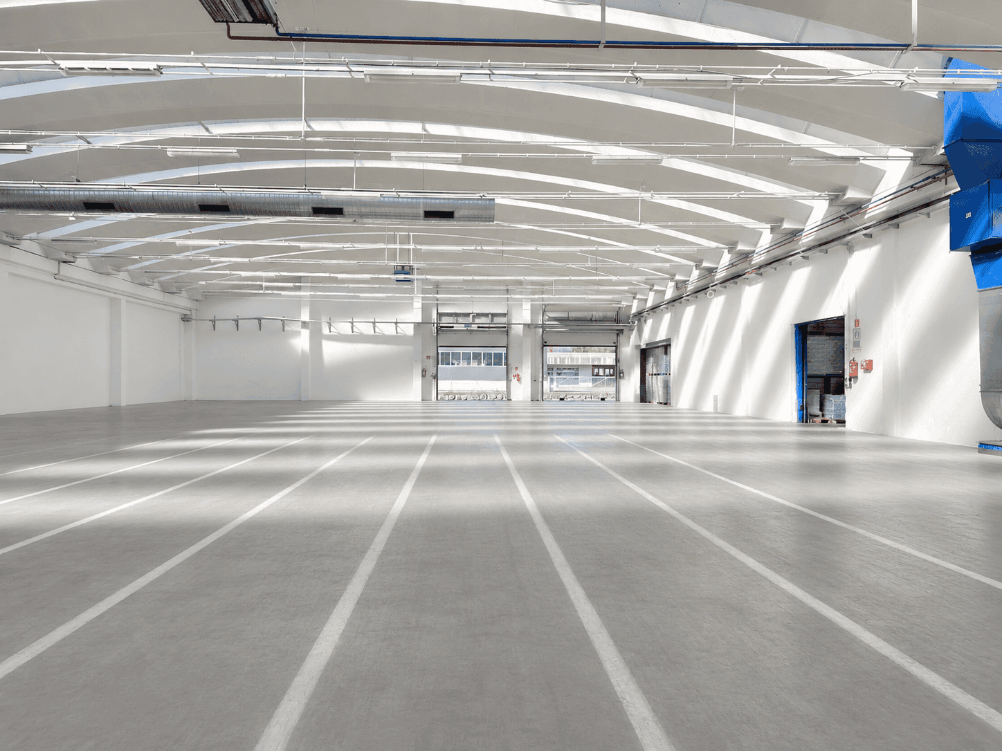 Helle und geräumige Lagerhalle mit Betonboden, hohen Decken und mehreren Toren für den Zugang.