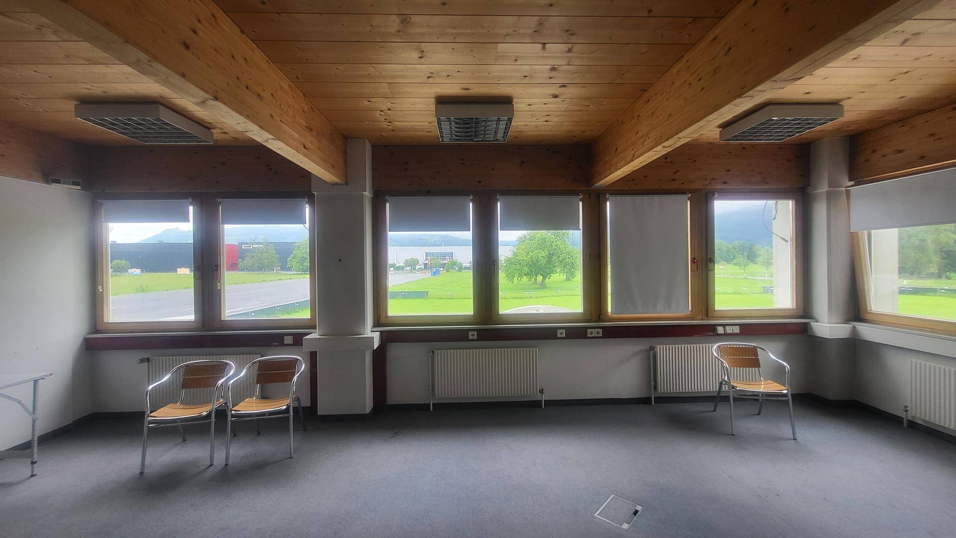 Heller Büroraum mit Holzbalkendecke, Panoramablick auf See und Berge sowie reichlich natürlichem Licht.