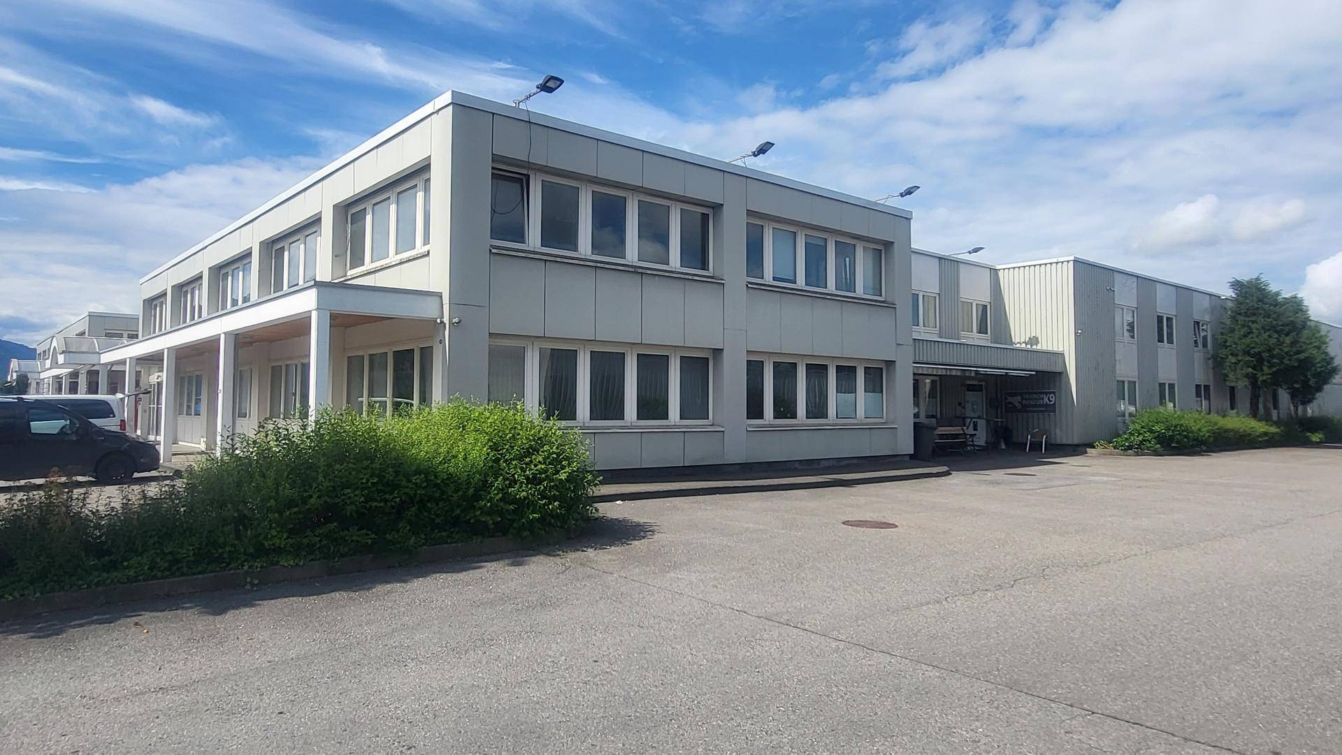 Modernes Geschäftsgebäude mit heller Fassade, großen Fenstern und ausreichend Parkplätzen im Freien.
