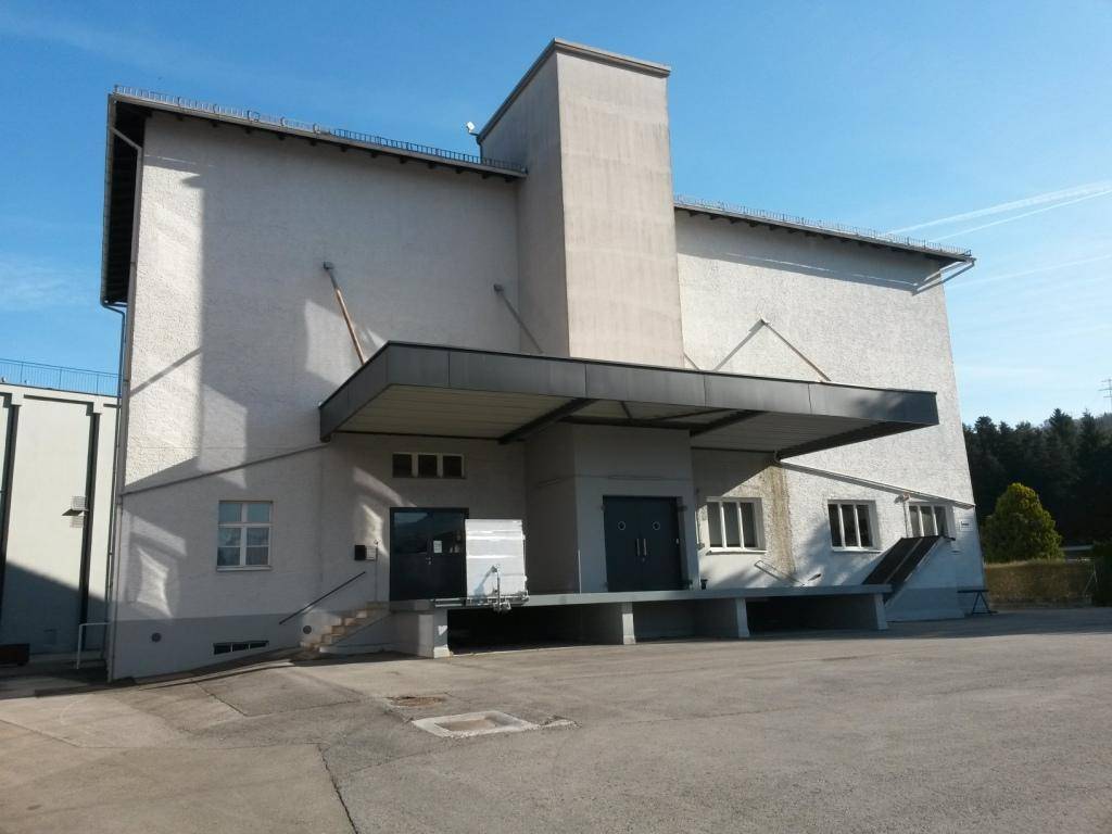 Außenansicht eines funktionalen Gewerbegebäudes mit Laderampe und großem Vorplatz unter blauem Himmel.