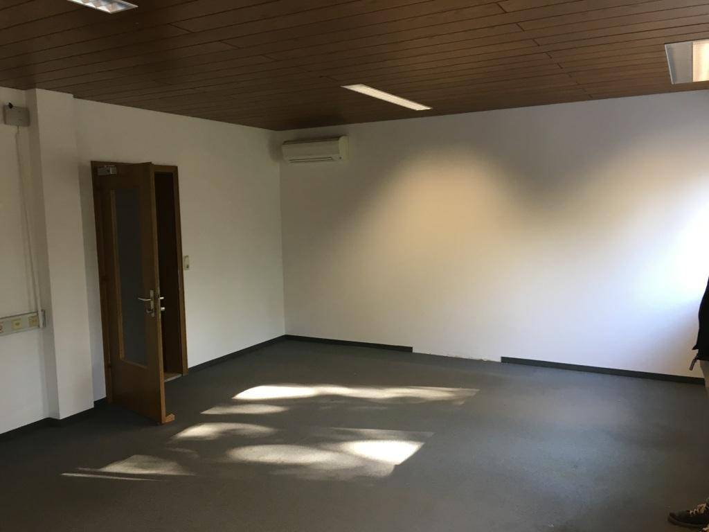Geräumiger Innenraum mit Holzdecke, Klimaanlage und grauem Teppichboden, beleuchtet von natürlichem Licht.