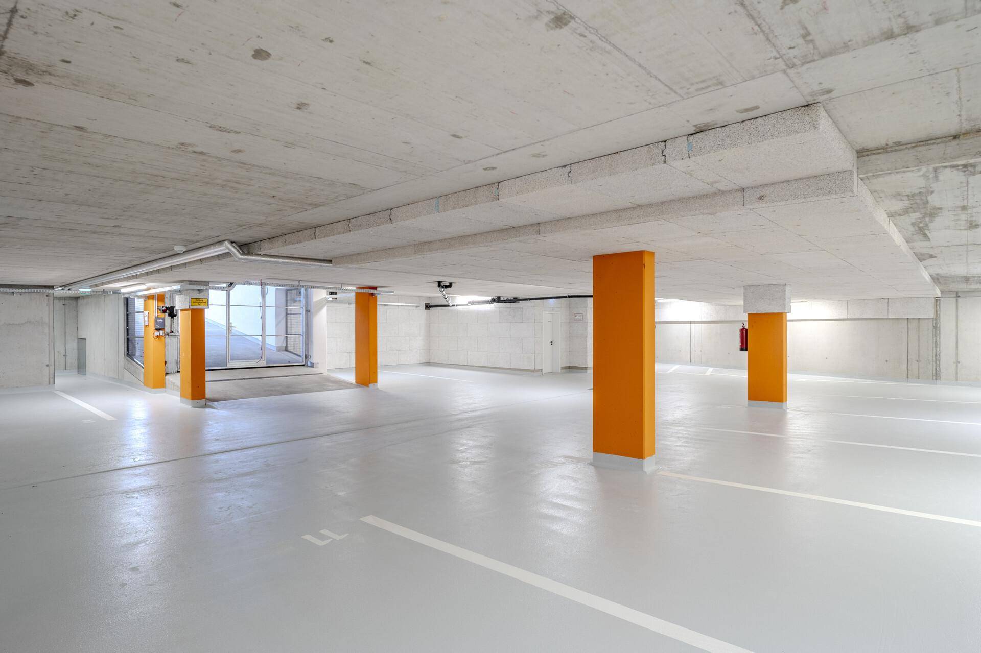 Geräumige Tiefgarage mit markierten Stellplätzen und orangefarbenen Säulen.